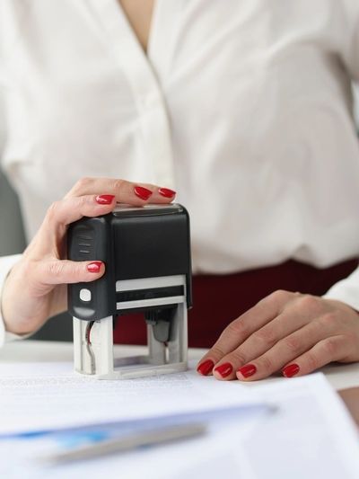 Person stamping a document with red-painted nails.